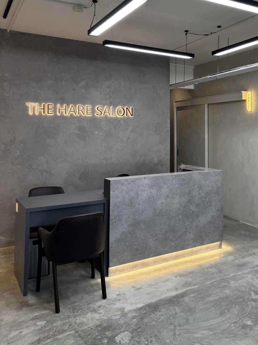 The Hare Salon reception — the gold signage above a warm-lit concrete desk and consultation table